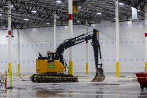 A full size excavator inside of the warehouse with a TuffWrap dust containment frameless wall behind the excavator