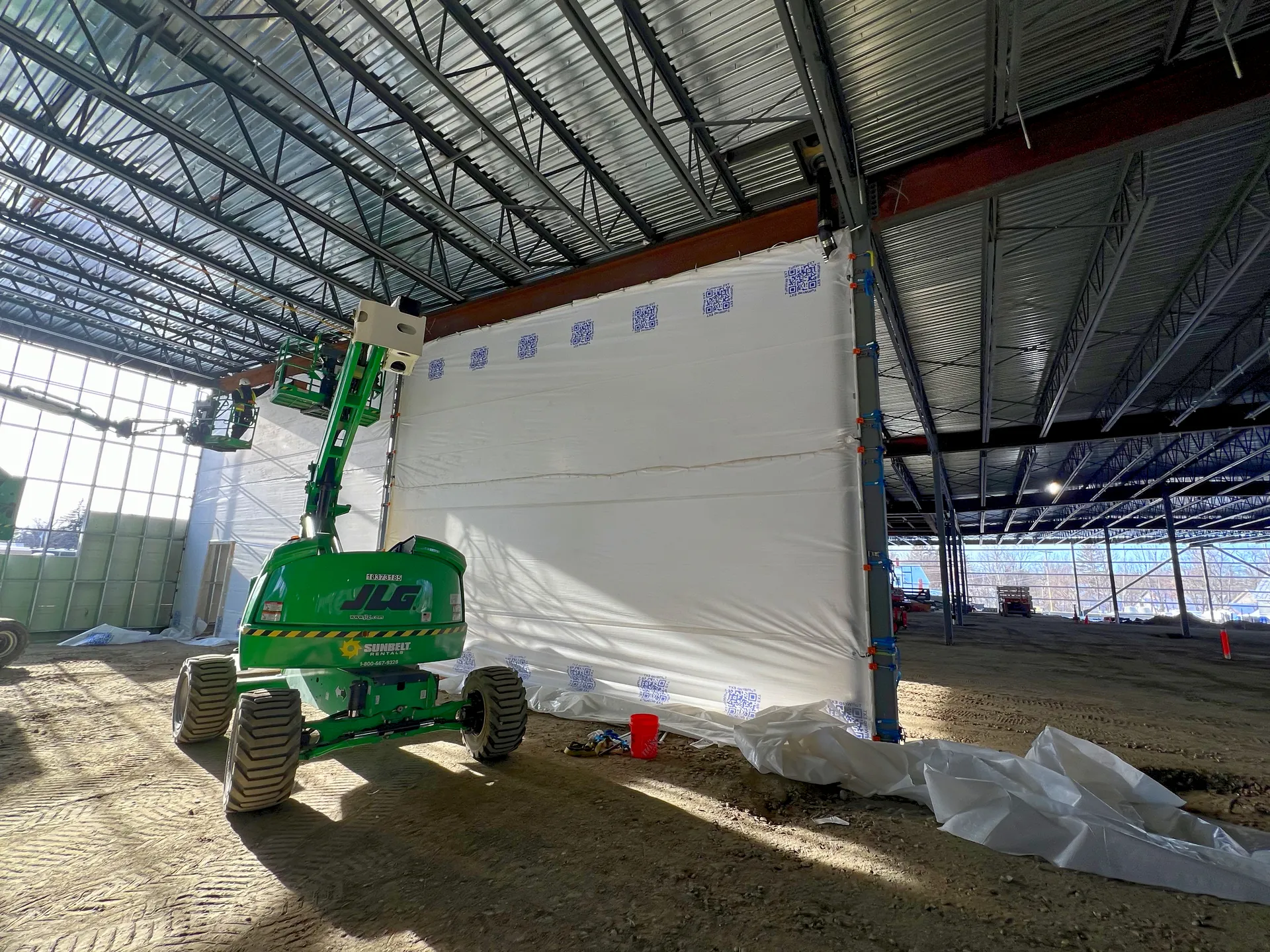 A work in progress picture of the installation. Two green JLG lifts working together to install the protection. 